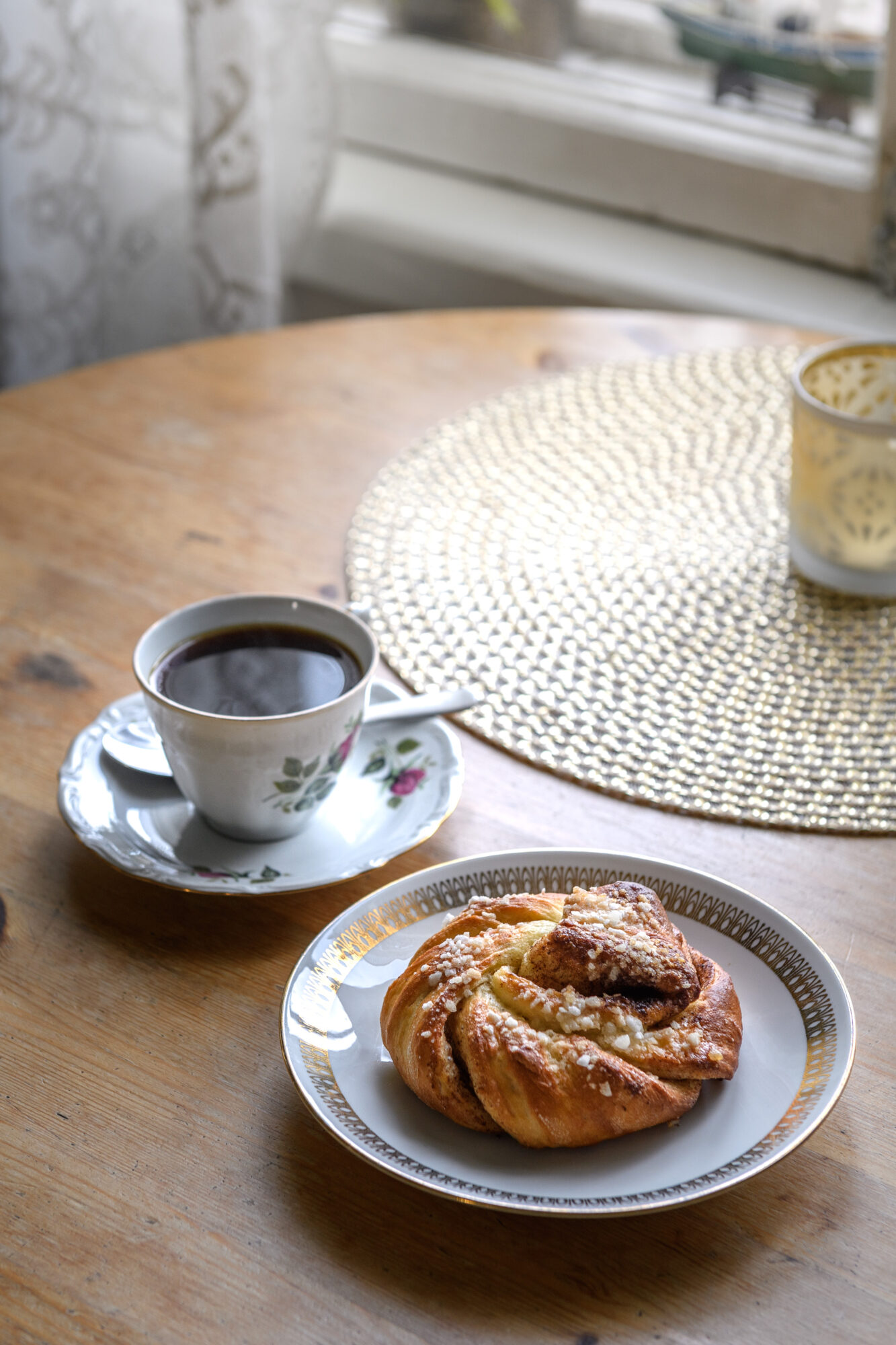 Black coffee and a cinnamon roll on a wooden round table.