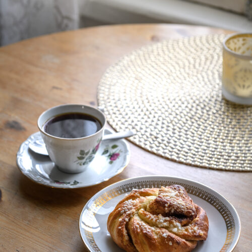 Black coffee and a cinnamon roll on a wooden round table.